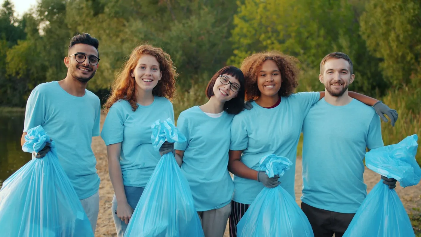 Five smiling volunteers in matching t-shirts holding filled bags after a community cleanup